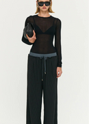 Model wearing a black outfit with sheer top and wide-leg stripe pants on a white background