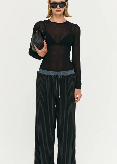 Model wearing a black outfit with sheer top and wide-leg stripe pants on a white background