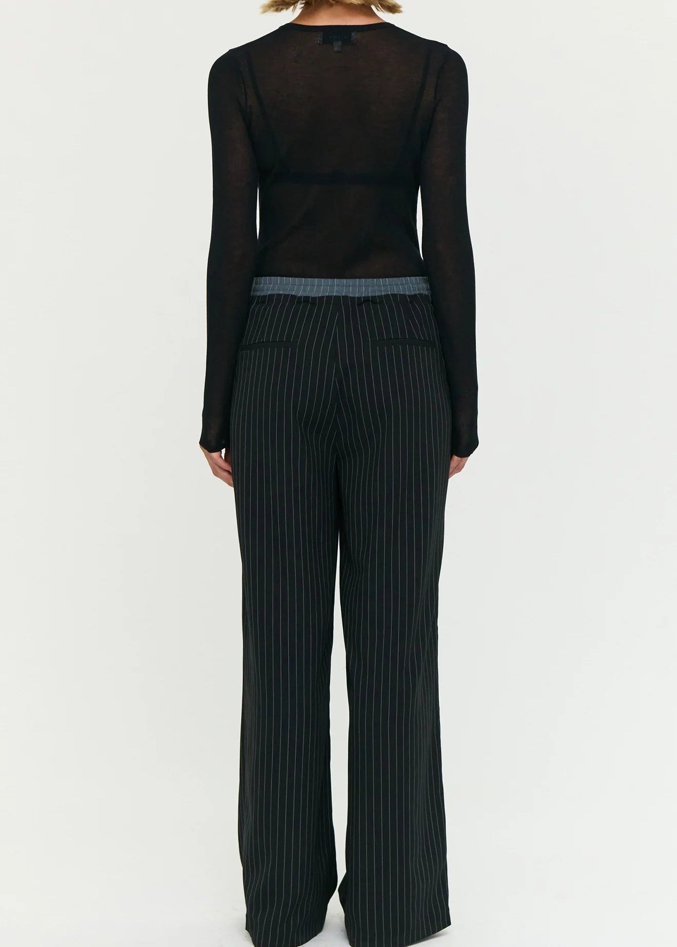 Model wearing a black outfit with sheer top and wide-leg stripe pants on a white background