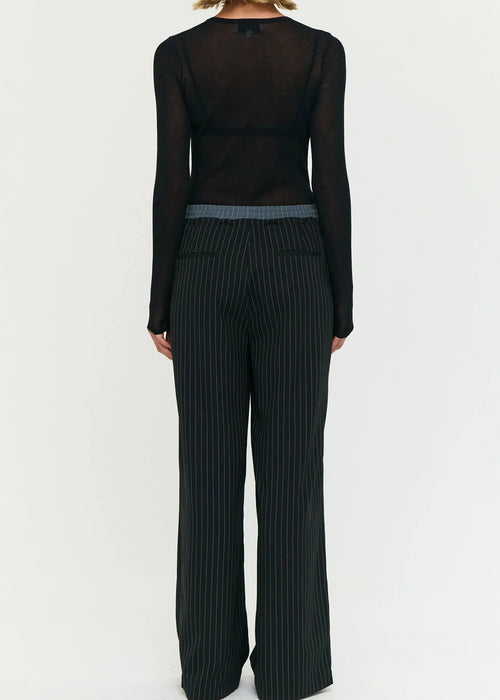 Model wearing a black outfit with sheer top and wide-leg stripe pants on a white background