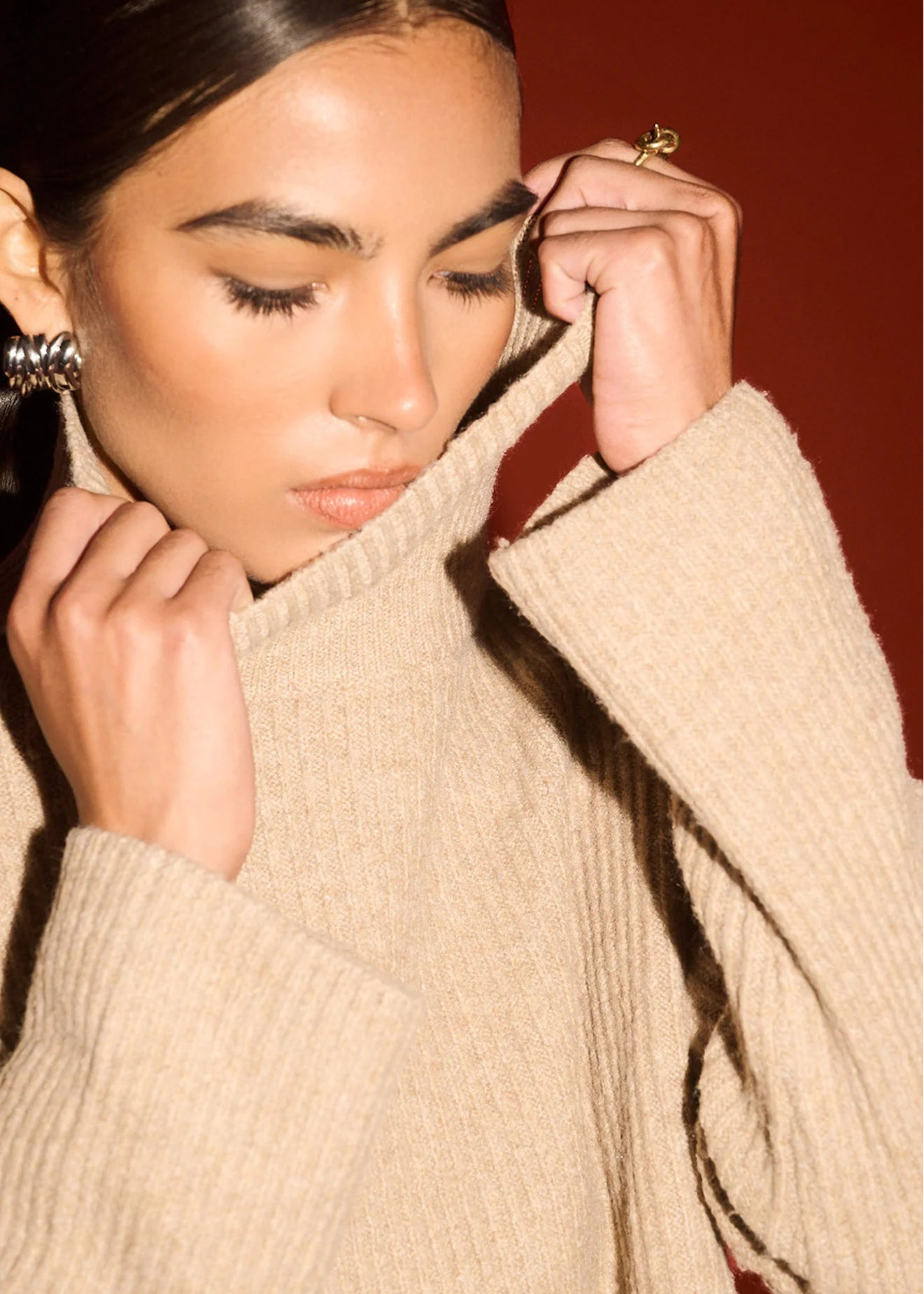 Woman wearing a beige turtleneck sweater against a red background