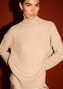 Woman wearing a beige turtleneck sweater against a red background