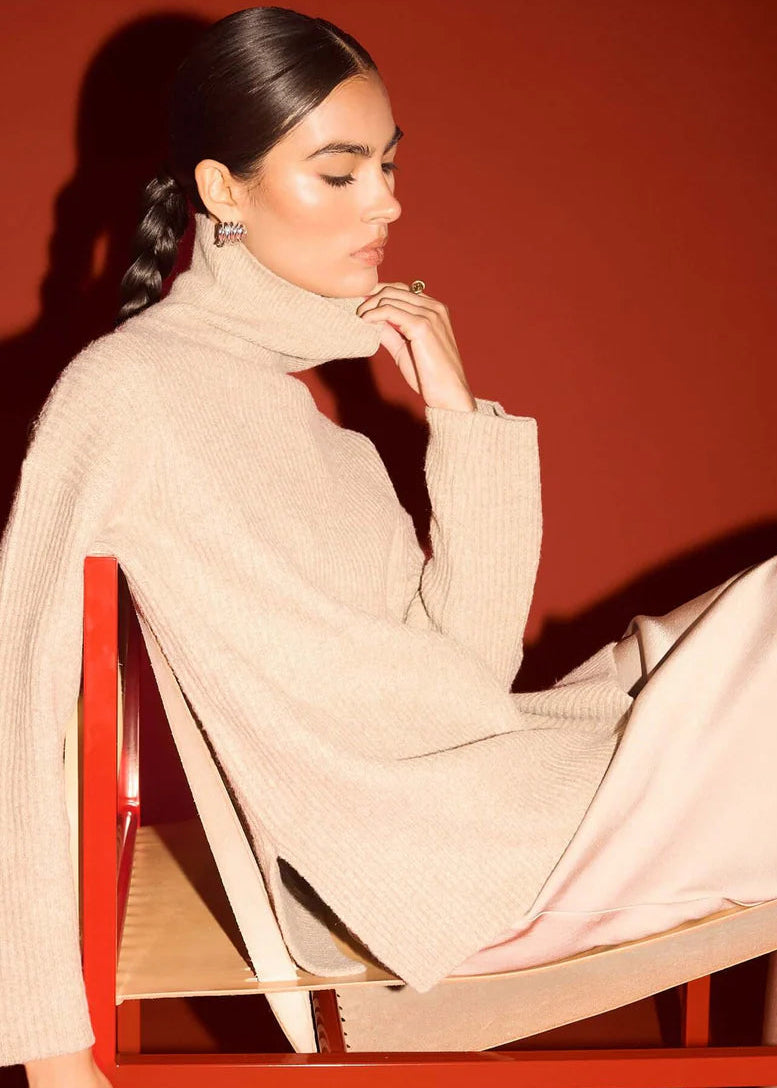 Woman wearing a beige turtleneck sweater against a red background
