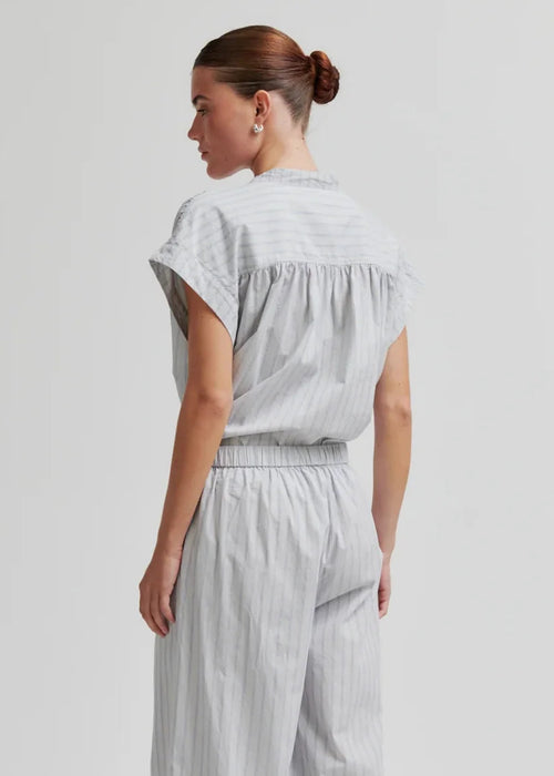 A woman shown from the back wearing a light grey and white vertically striped short-sleeve top and matching wide-leg pants, paired with black flip-flops, against a light grey studio background.