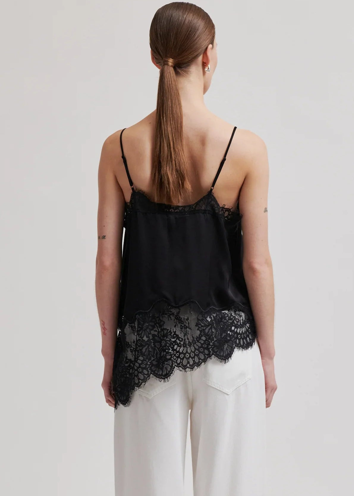 Woman wearing a black lace top and white pants on a plain background
