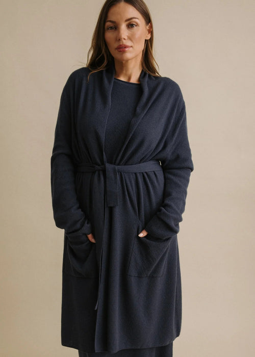 Woman wearing a navy blue cardi with a belt against a beige background