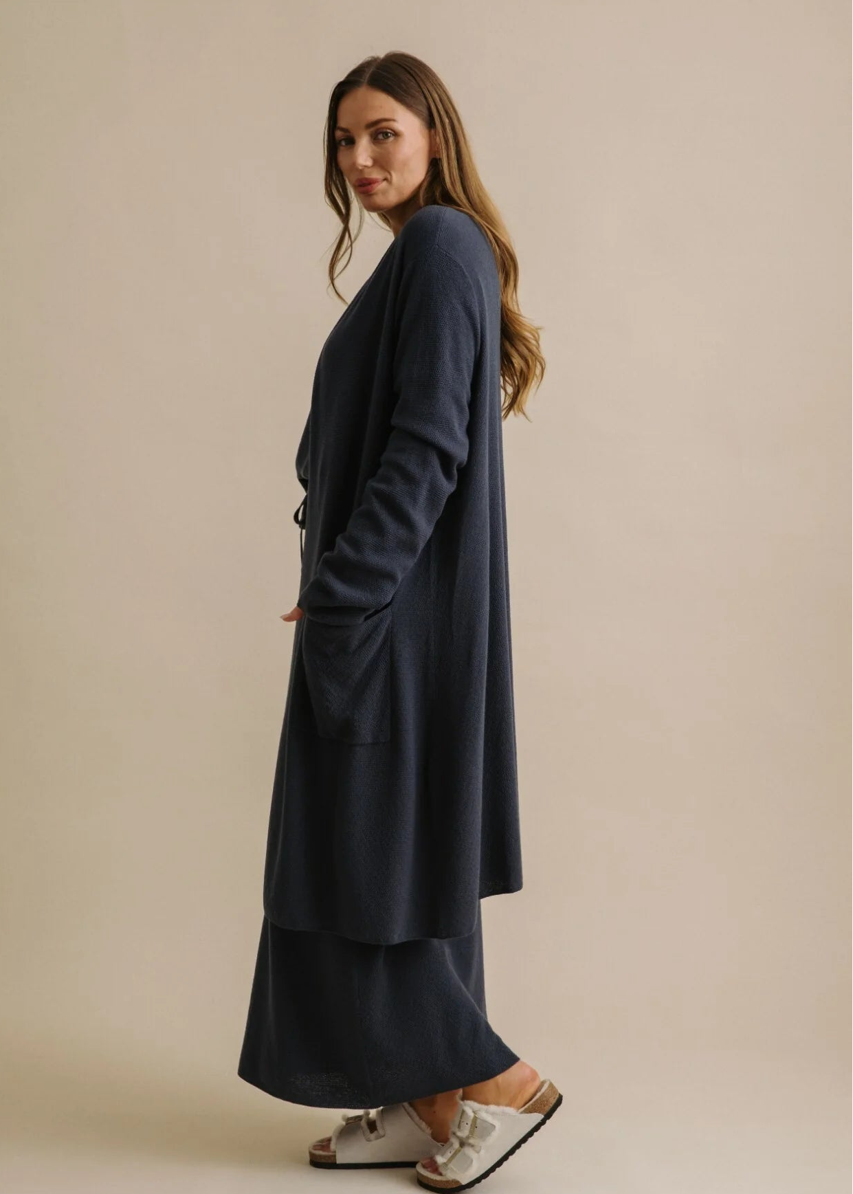Woman wearing a navy blue cardi with a belt against a beige background