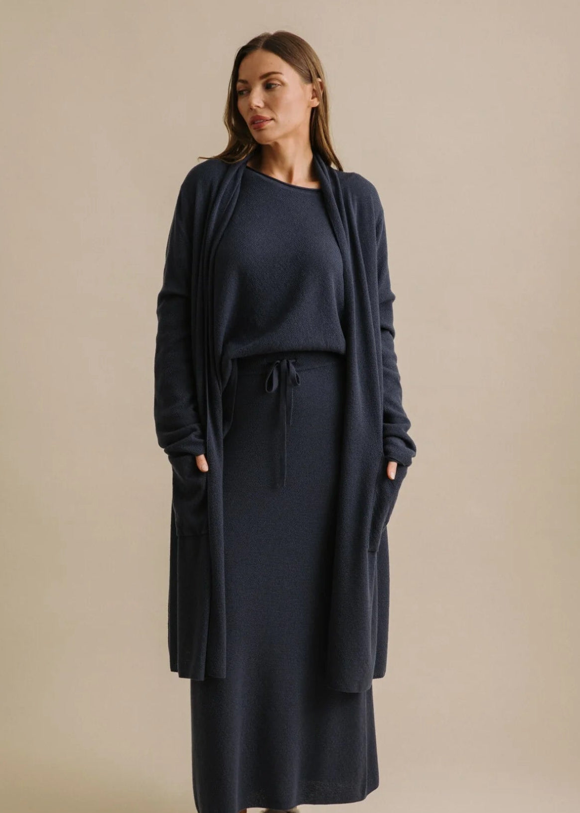 Woman wearing a navy blue cardi with a belt against a beige background
