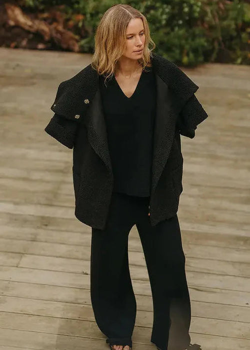 Woman in a black outfit standing outdoors with a neutral background