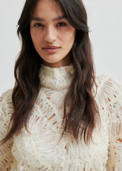 Woman wearing a textured white blouse against a plain background