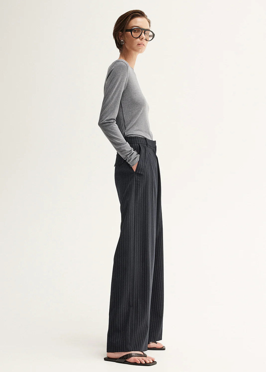 Woman wearing a grey sweater and black pinstripe pants on a white background