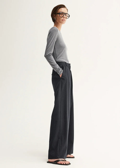 Woman wearing a grey sweater and black pinstripe pants on a white background