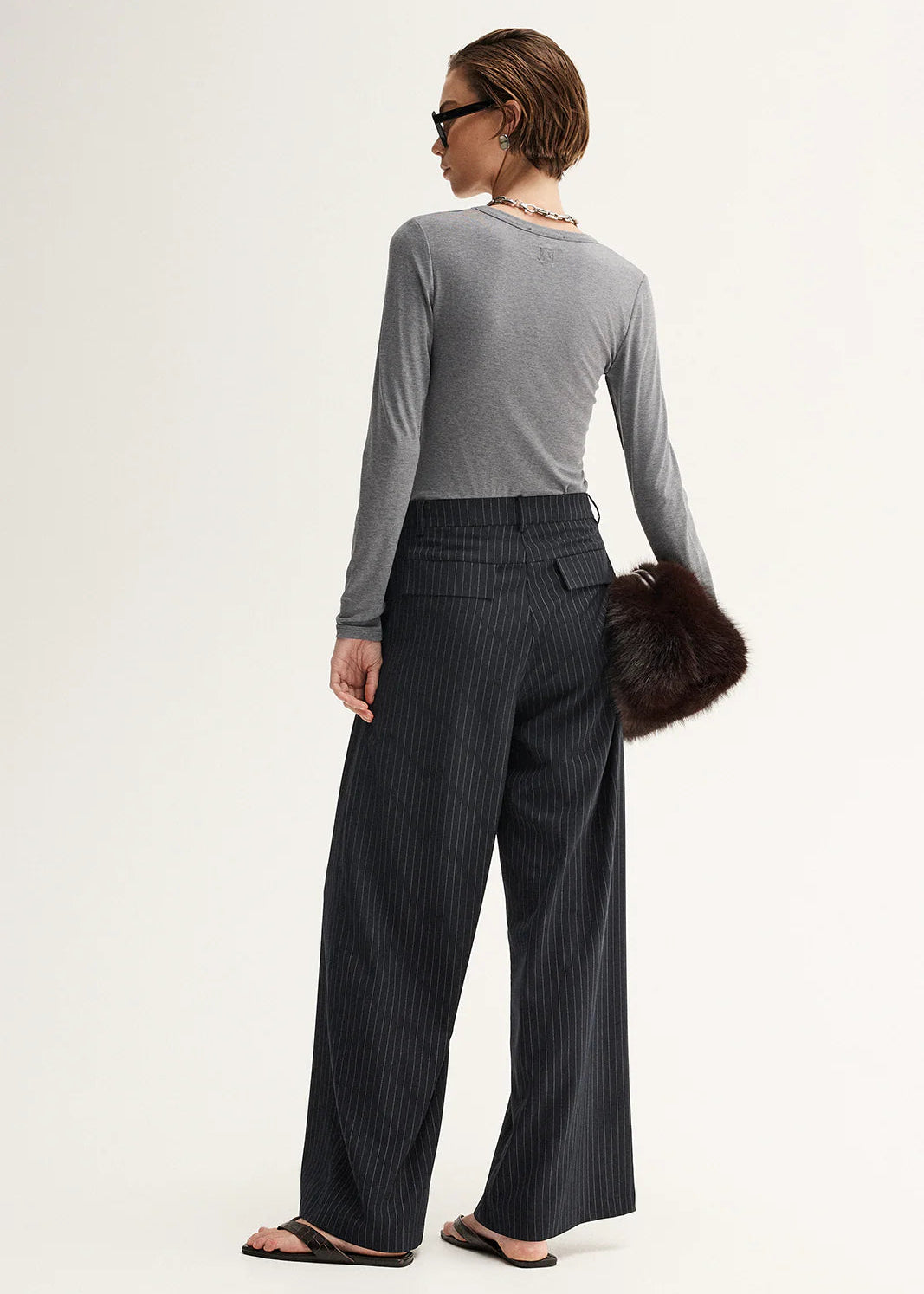 Woman wearing a grey sweater and black pinstripe pants on a white background