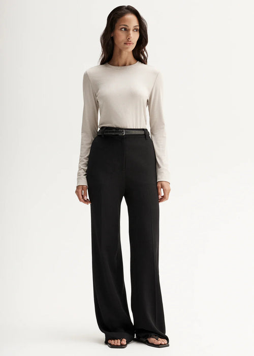 Woman wearing a white long-sleeve top and black pants on a white background