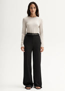 Woman wearing a white long-sleeve top and black pants on a white background