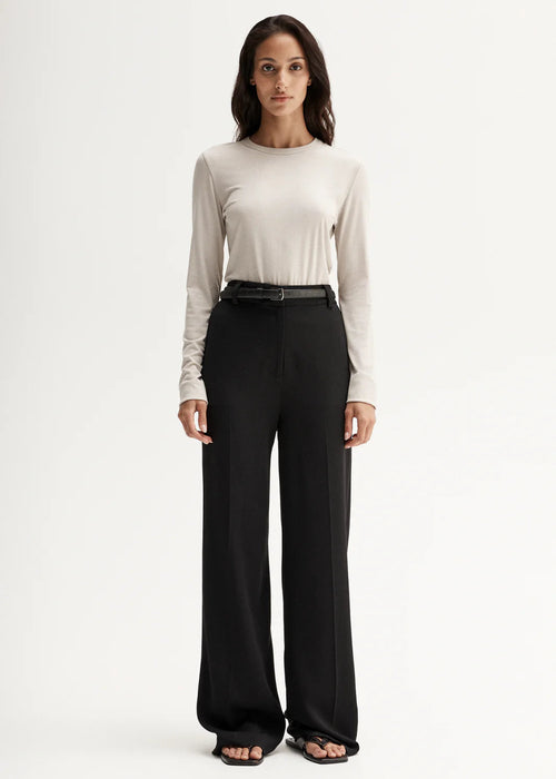 Woman wearing a white long-sleeve top and black pants on a white background