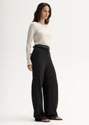 Woman wearing a white long-sleeve top and black pants on a white background