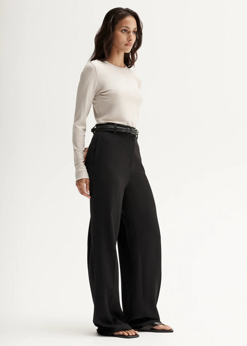 Woman wearing a white long-sleeve top and black pants on a white background