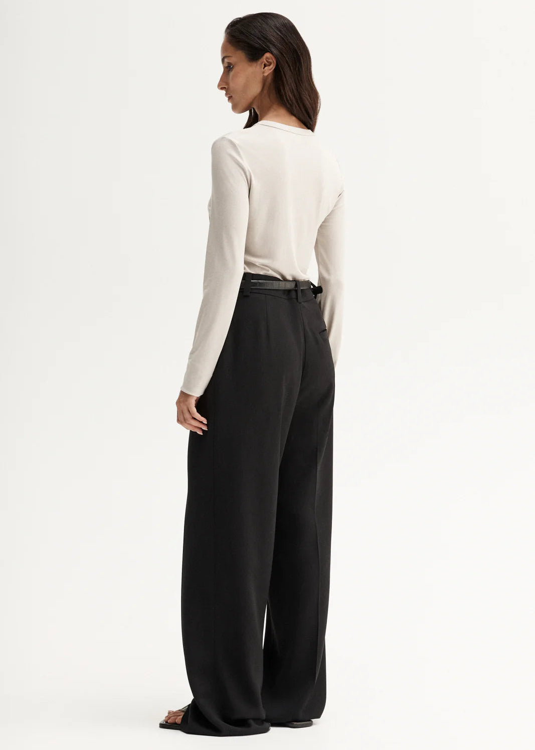 Woman wearing a white long-sleeve top and black pants on a white background