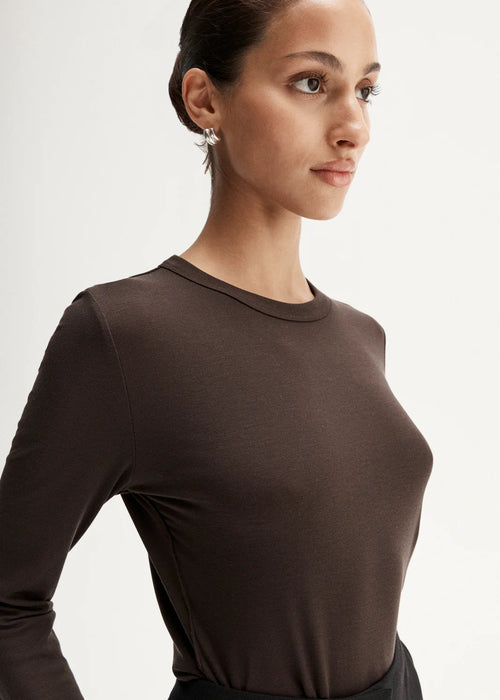 Woman wearing a brown long-sleeve top and black high-waisted pants, holding a black handbag on a white background.
