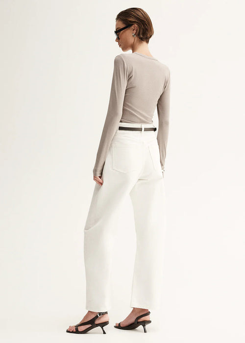 Woman wearing a grey long-sleeve top and white pants on a white background