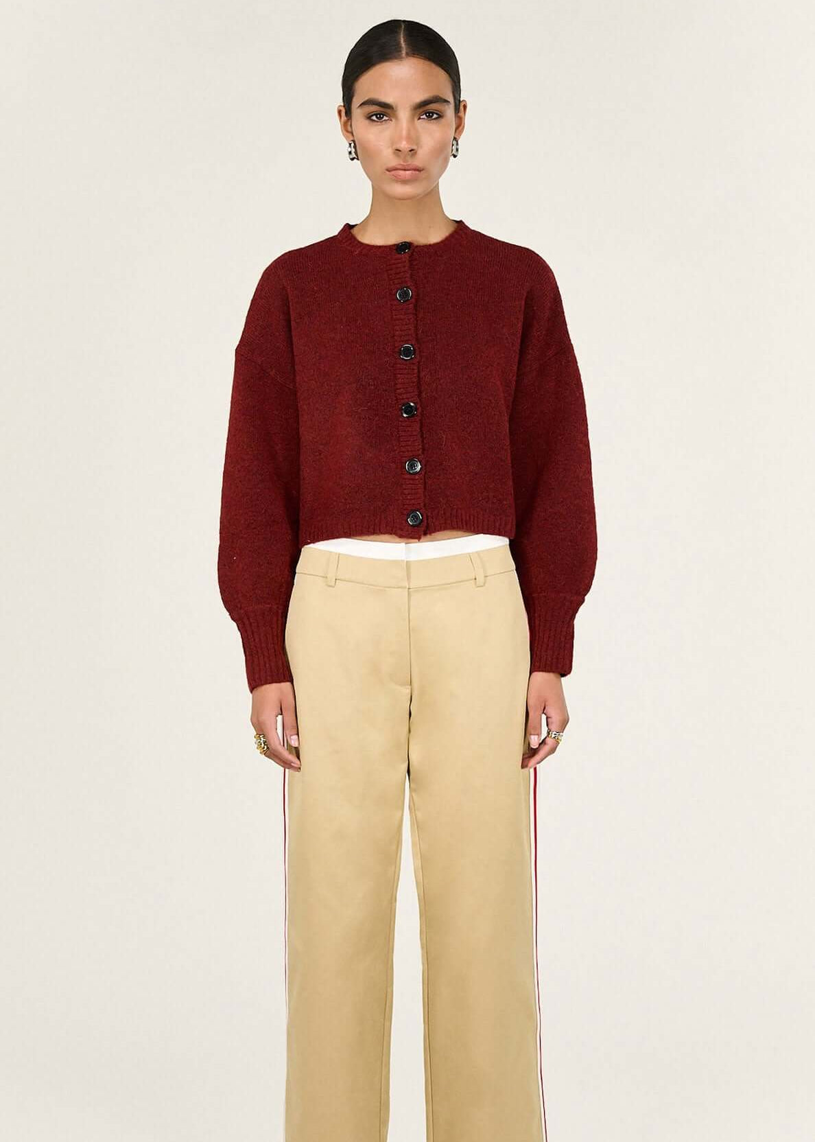 Woman wearing a burgundy cardigan and beige pants on a white background