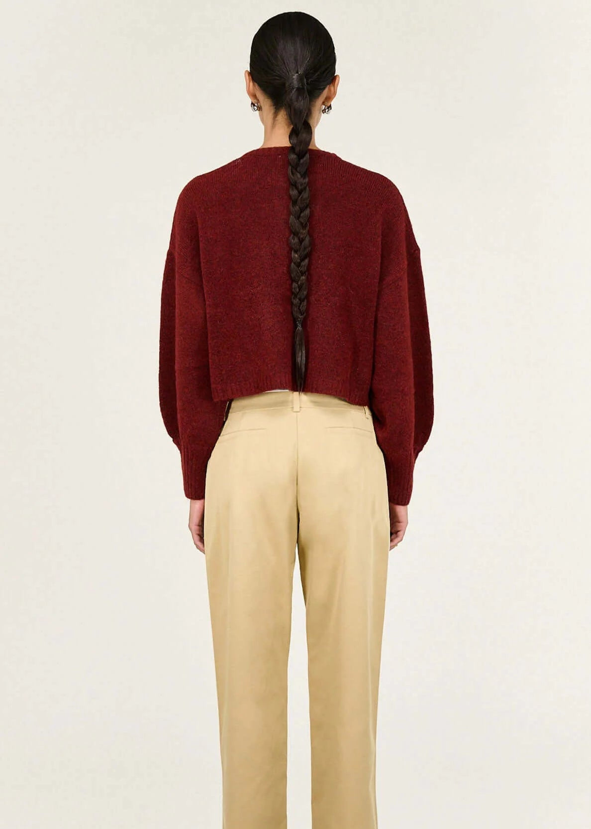 Woman wearing a burgundy cardigan and beige pants on a white background