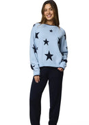 Woman wearing a light blue sweater with black star patterns and dark pants on a white background