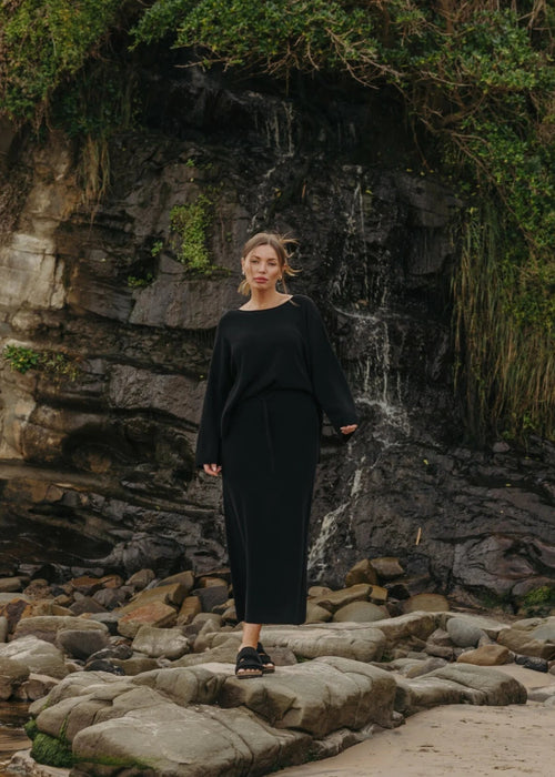 Woman in a black outfit standing on rocks with a waterfall in the background