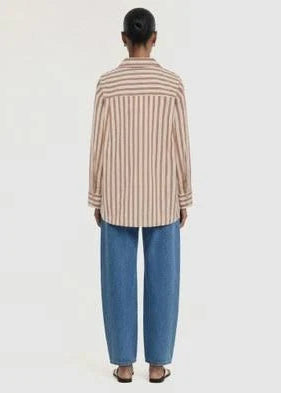 A model viewed from behind wearing a beige and brown vertically striped button-up shirt and wide-leg blue jeans against a plain white background.
