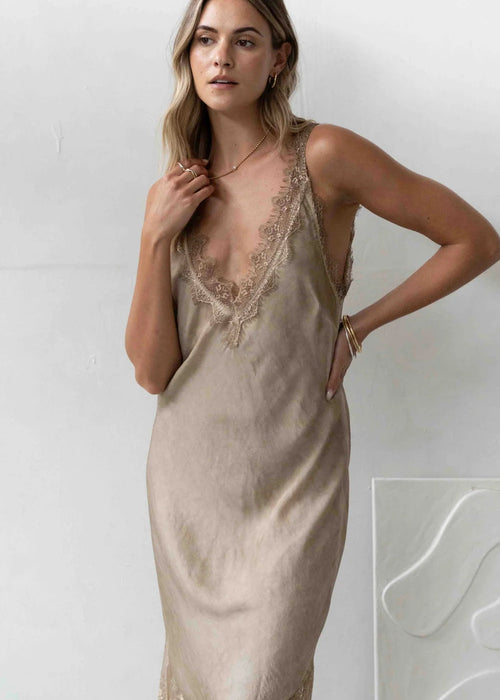 Woman wearing a beige slip dress with lace details against a white background