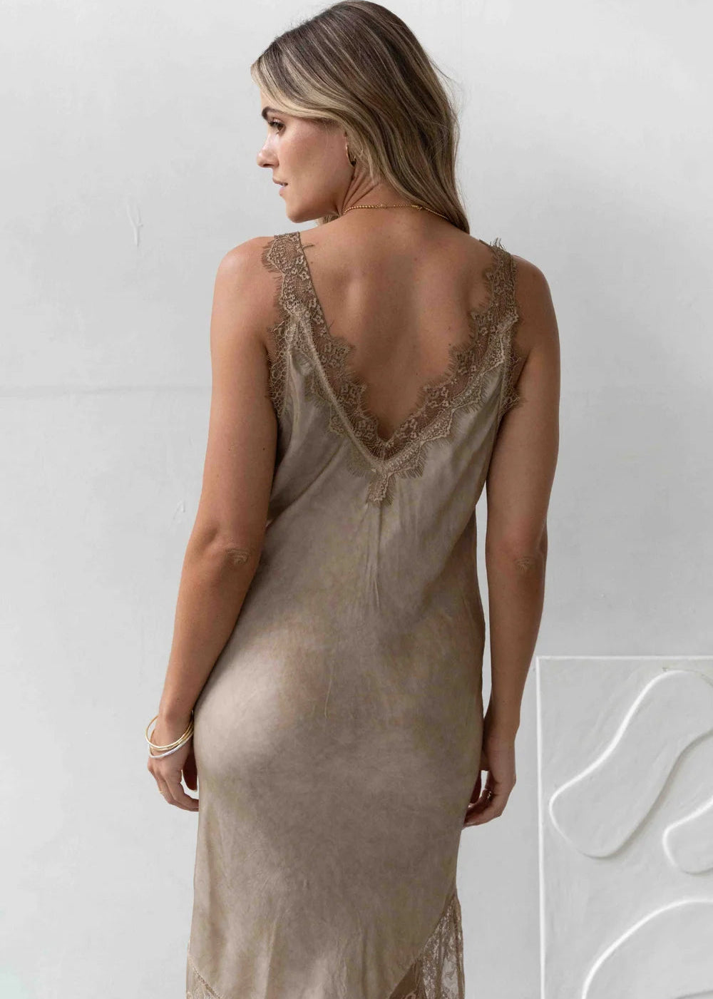 Woman wearing a beige slip dress with lace details against a white background