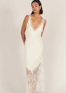 A woman modelling a cream lace slip dress  set against a solid light beige studio background.