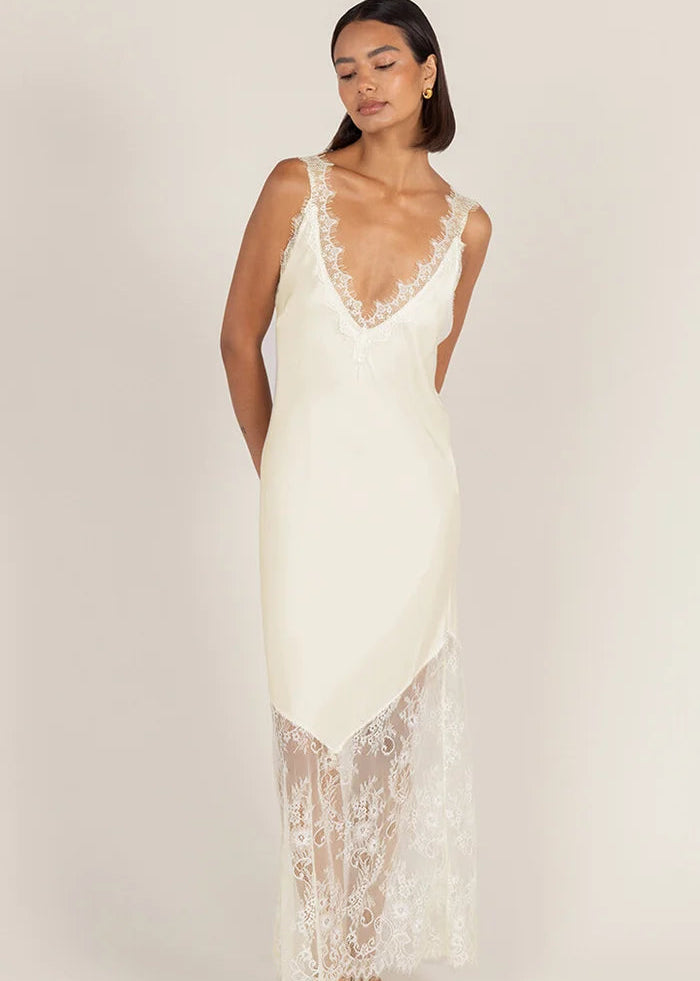 A woman modelling a cream lace slip dress  set against a solid light beige studio background.