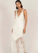 A woman modelling a cream lace slip dress  set against a solid light beige studio background.