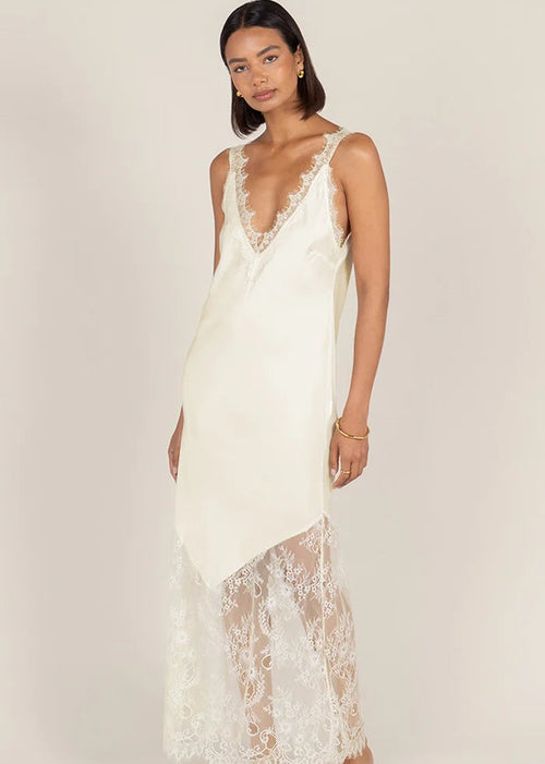 A woman modelling a cream lace slip dress  set against a solid light beige studio background.