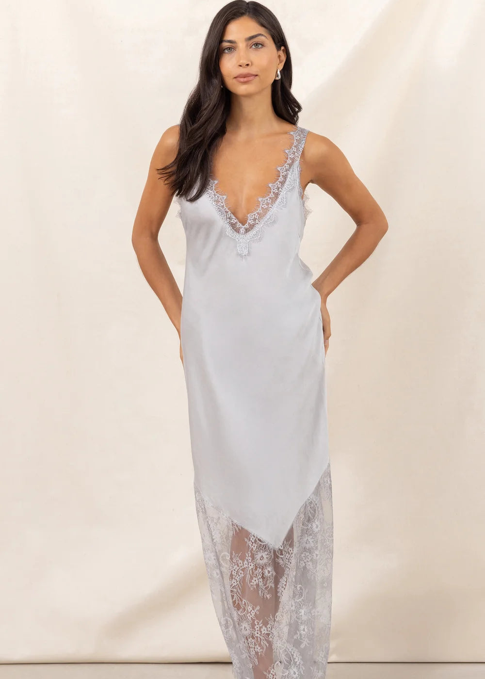 Woman wearing a opaque white slip dress with lace details against a plain background