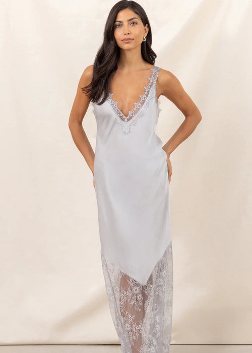 Woman wearing a opaque white slip dress with lace details against a plain background