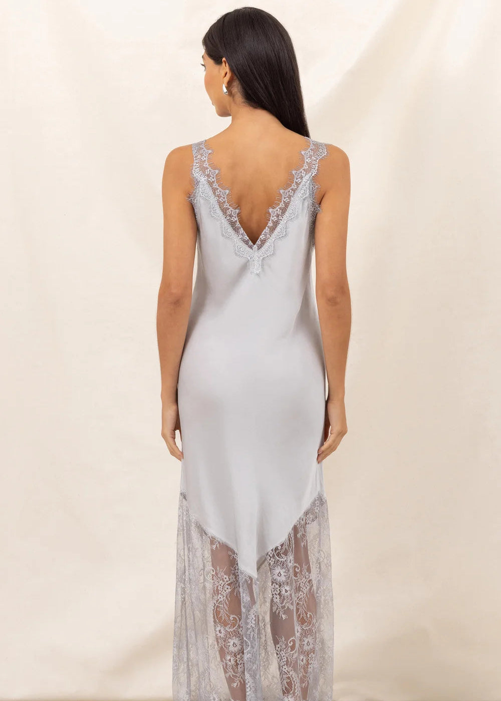 Woman wearing a opaque white slip dress with lace details against a plain background