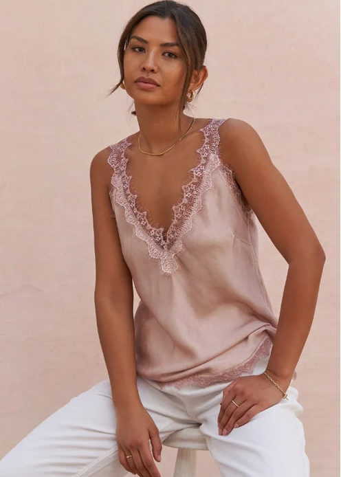 Woman wearing a pink lace-trimmed top against a light pink background
