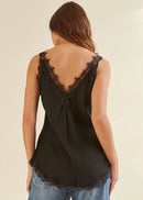Woman wearing a black sleeveless top with lace details on a beige background