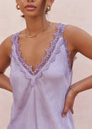 Woman wearing a light purple lace-trimmed top against a beige background