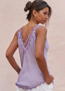 Woman wearing a light purple lace-trimmed top against a beige background
