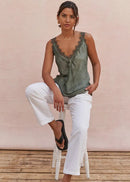 Woman wearing a green sleeveless top and white pants sitting on a wooden floor