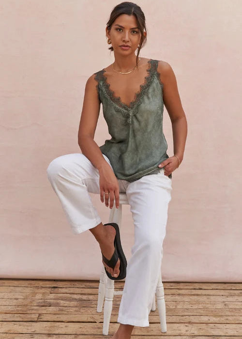 Woman wearing a green sleeveless top and white pants sitting on a wooden floor