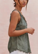 Woman wearing a green sleeveless top and white pants sitting on a wooden floor