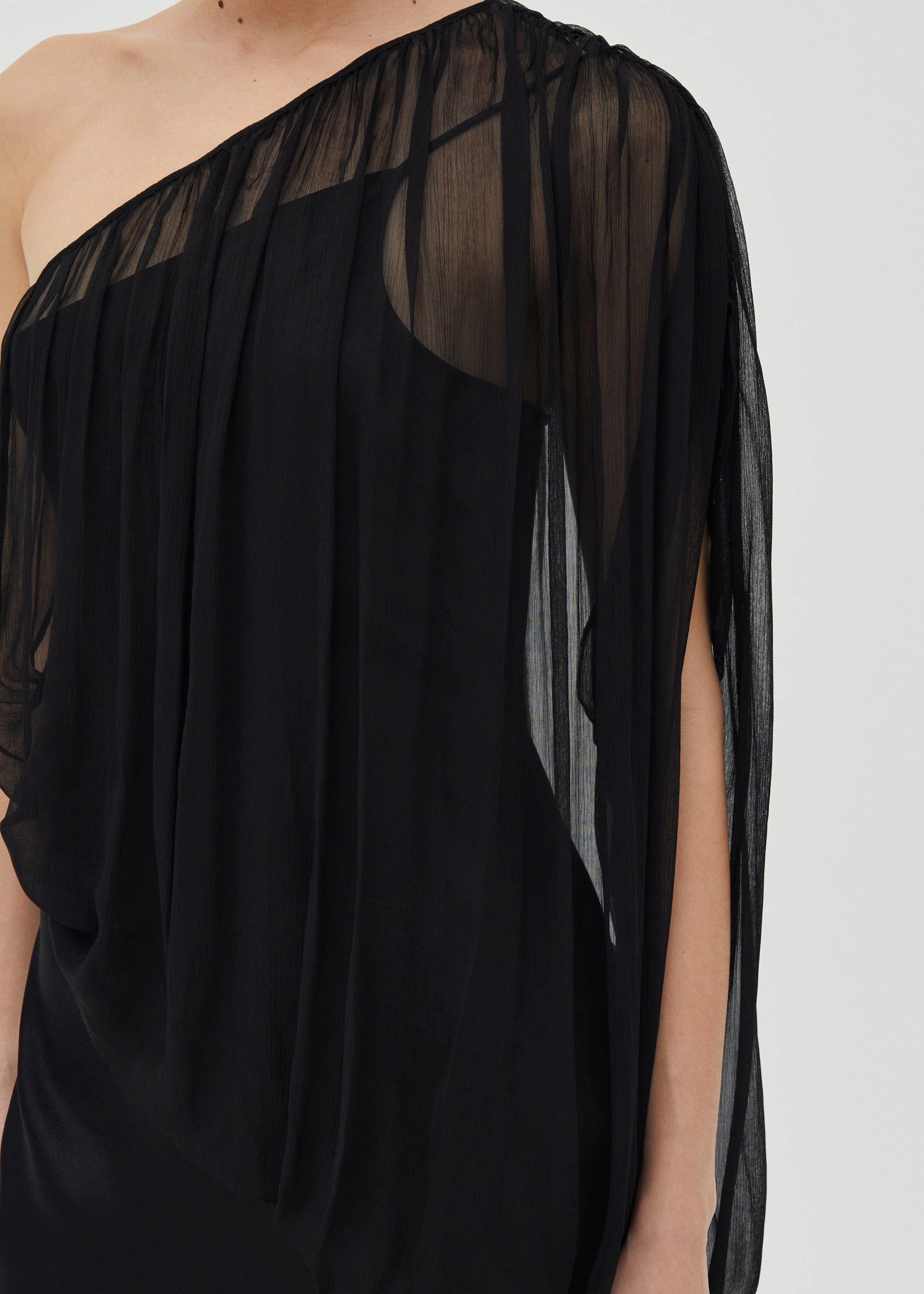 Black one-shoulder dress with sheer sleeves on a white background