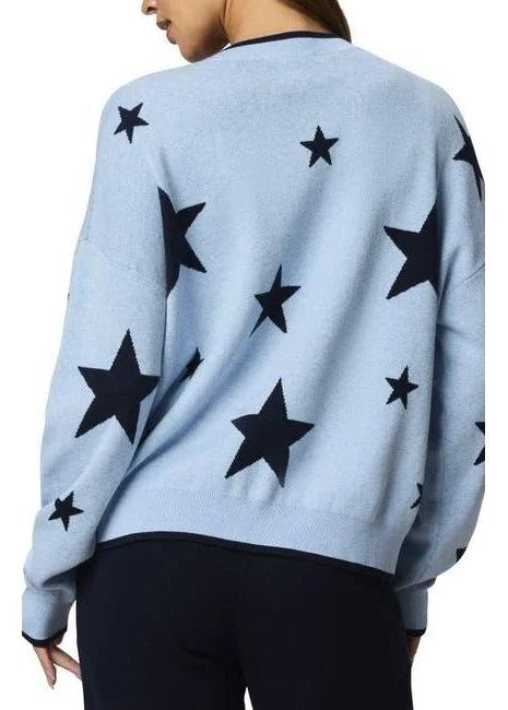 Woman wearing a light blue sweater with black star patterns and dark pants on a white background