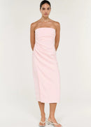 A woman modelling a pale pink strapless midi dress with gathered draping at the waist, photographed against a clean off-white studio background.