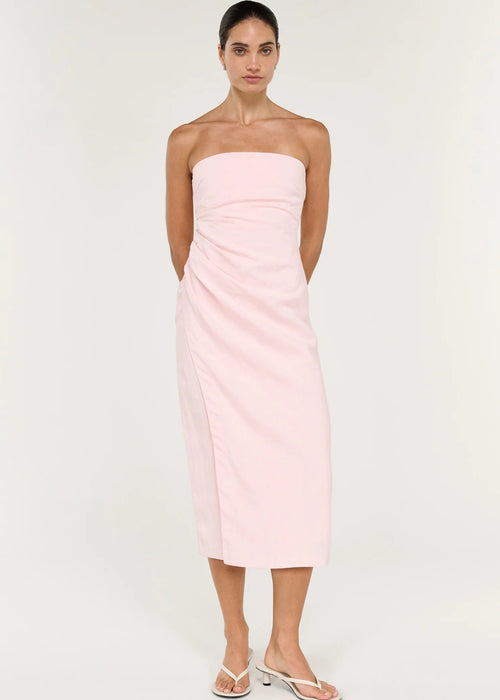 A woman modelling a pale pink strapless midi dress with gathered draping at the waist, photographed against a clean off-white studio background.